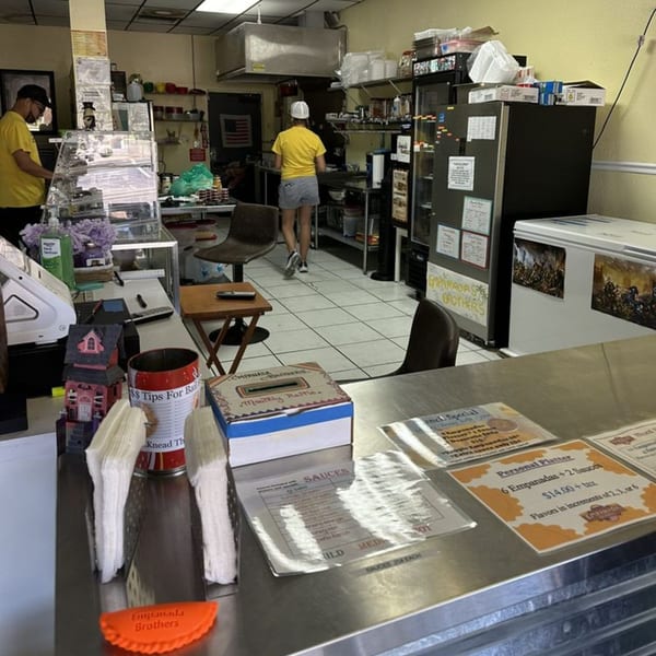 Interior of Empanada Brothers, showing a counter with menus, a tip jar, and staff working in the kitchen.