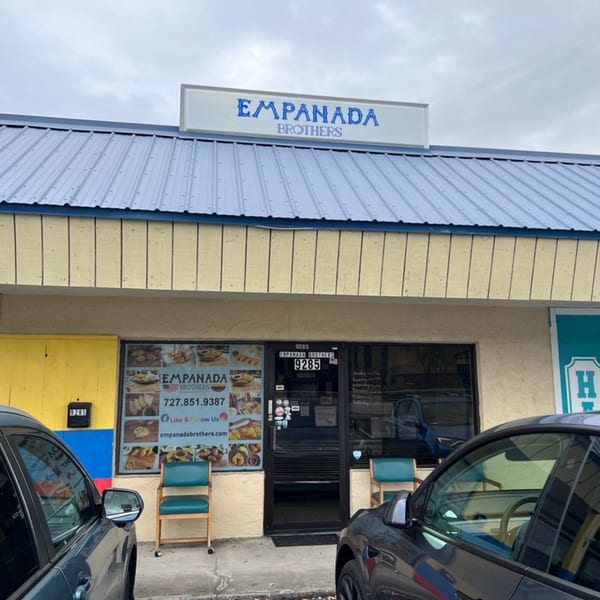 Exterior of Empanada Brothers restaurant with a blue roof, yellow facade, and cars parked in front.