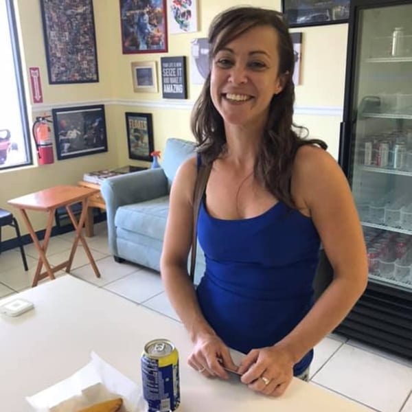 Smiling woman in a blue top standing at a table with a drink and food at Empanada Brothers.