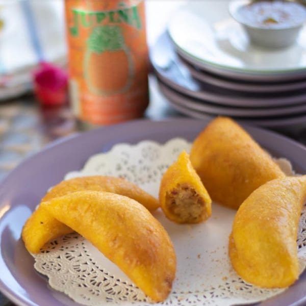 Golden Colombian empanadas on a purple plate with a Jupiña soda can in the background.