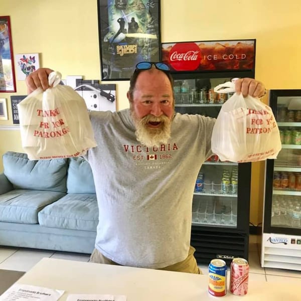 A smiling man holds two Empanada Brothers takeout bags, with Colombian sodas on the counter.