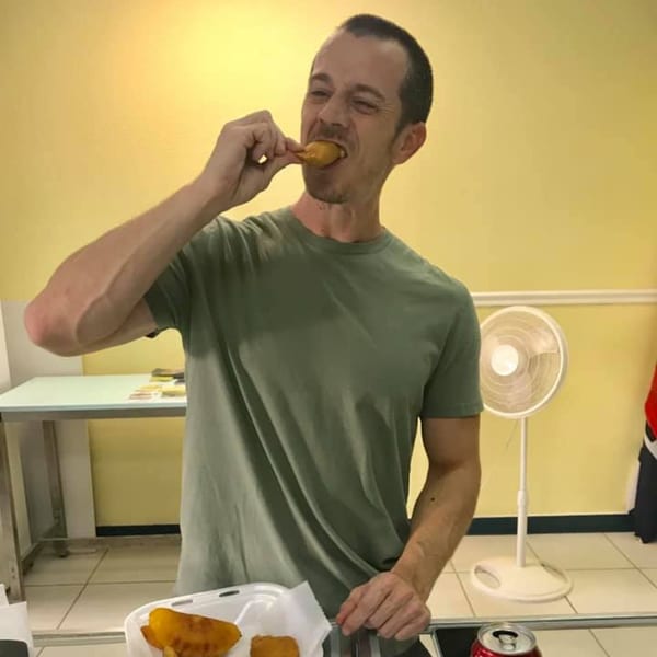 A man in a green shirt happily eats a Colombian empanada from a takeout container.