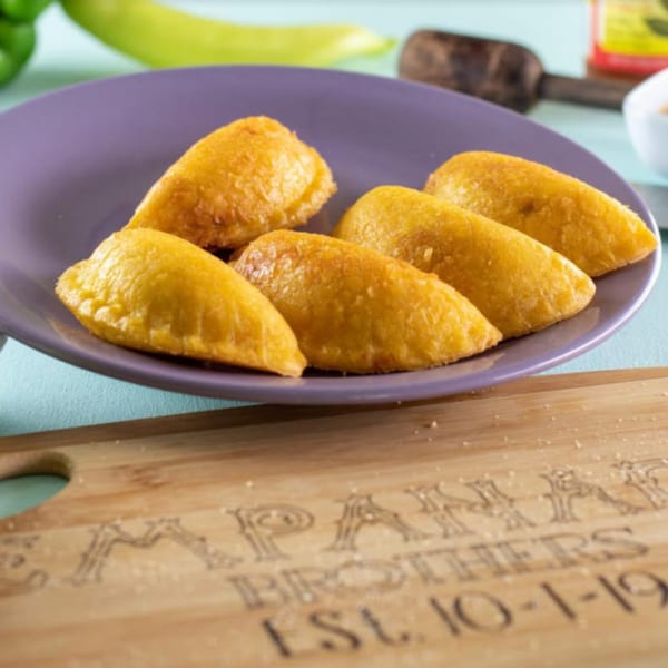Six golden-brown Empanada Brothers empanadas on a purple plate, with a branded wooden board below.