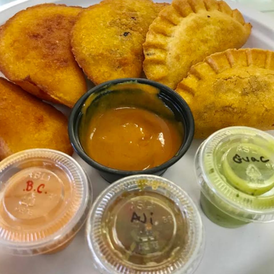 Golden Colombian empanadas with various dipping sauces, including aji and guacamole.