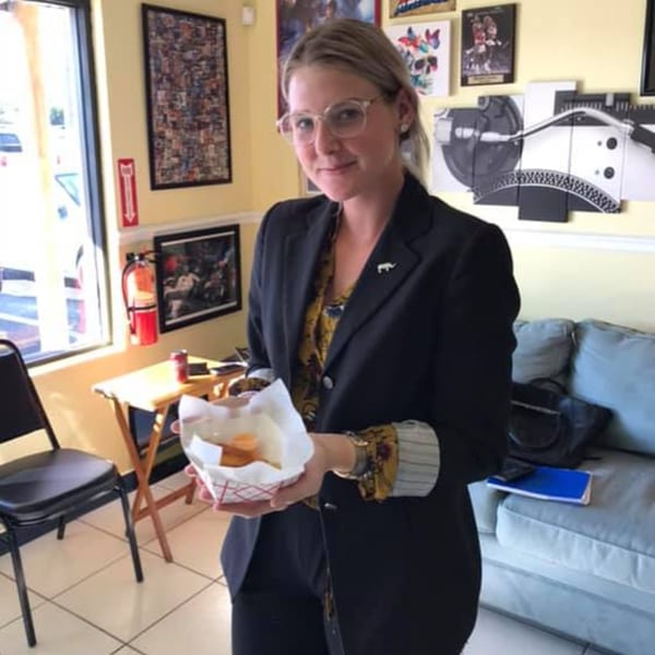 Woman in glasses and a blazer holding a basket of Empanada Brothers' Colombian empanadas.